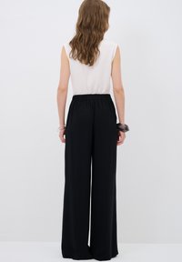 Zwarte wijde broeken met een elastische tailleband, een zachte textuur en een relaxte pasvorm. Gecombineerd met een mouwloze, lichtgekleurde top.