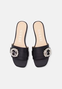 Infradito in satin nero con una fibbia in strass chunky e dettagli con più cinturini. Presenta una soletta beige con il nome del marchio "GUESS."