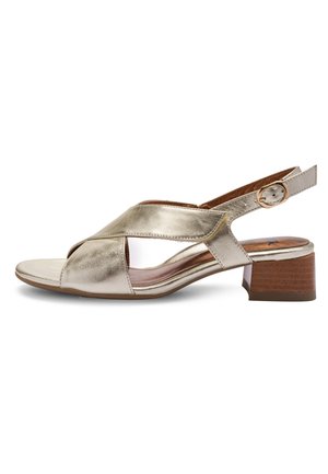 Slingback sandál s kovově zlatými koženými pásky, malým blokovým dřevěným podpatkem a zlatou přezkou na bílém pozadí.