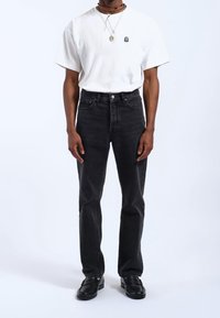 Jeans de mezclilla negra y una camiseta de algodón blanca con un pequeño logo, combinadas con mocasines negros. El ajuste es relajado y el tejido es suave.
