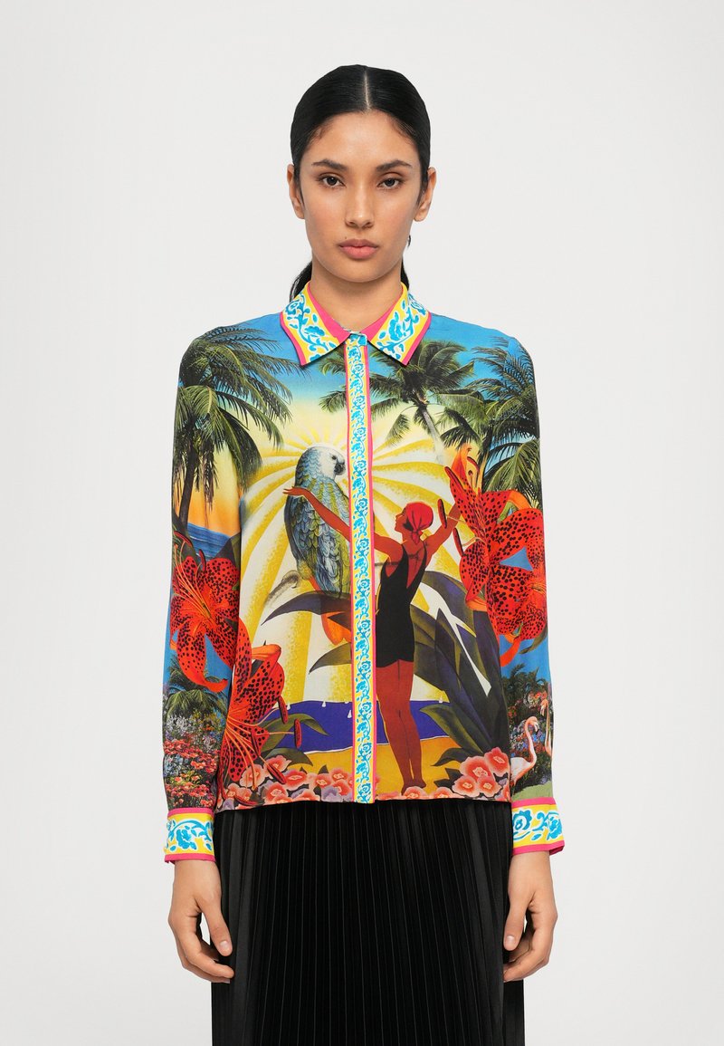 Blouse colorée à imprimé avec motif tropical, comprenant des fleurs et un perroquet. Col de chemise en bleu et rose ; manches longues avec des poignets vibrants.