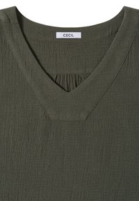 Blouse texturée vert olive foncé avec encolure en V, présentant de légers fronces sous l'encolure et une étiquette de marque "CECIL" à l'intérieur du col.