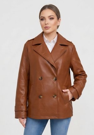 Kobieta w brązowej dwurzędowej skórzanej kurtce, białej koszuli i niebieskich dżinsach, z jedną ręką w kieszeni kurtki.