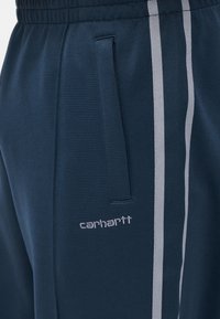 Παντελόνια φόρμας σε ναυτικό μπλε χρώμα από απαλό ύφασμα, με γκρι πλευρική ρίγα, ελαστική μέση και πλαϊνές τσέπες με κεντημένο λογότυπο "carhartt".