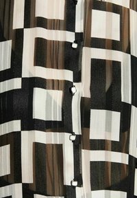 Blusa trasparente con un motivo geometrico bianco e nero, caratterizzata da righe verticali e bottoni quadrati. Tessuto morbido e leggero.