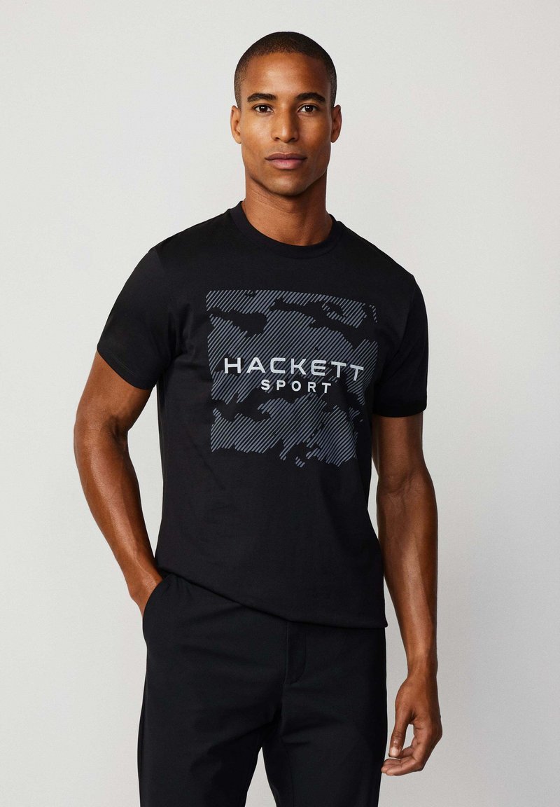 Camiseta negra de manga corta con un patrón gráfico y el texto "HACKETT SPORT" en blanco. El material parece suave y con una textura lisa.