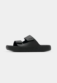 Chanclas negras de slide con suela de goma texturizada, correas de Velcro ajustables y un diseño minimalista con la marca "VEJA" embellecida.