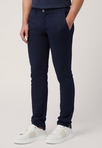 Náměrkové slim-fit chinos v hladké bavlněné tkanině, s bočními kapsami a předním zapínáním na knoflík. V kombinaci s bílými teniskami.
