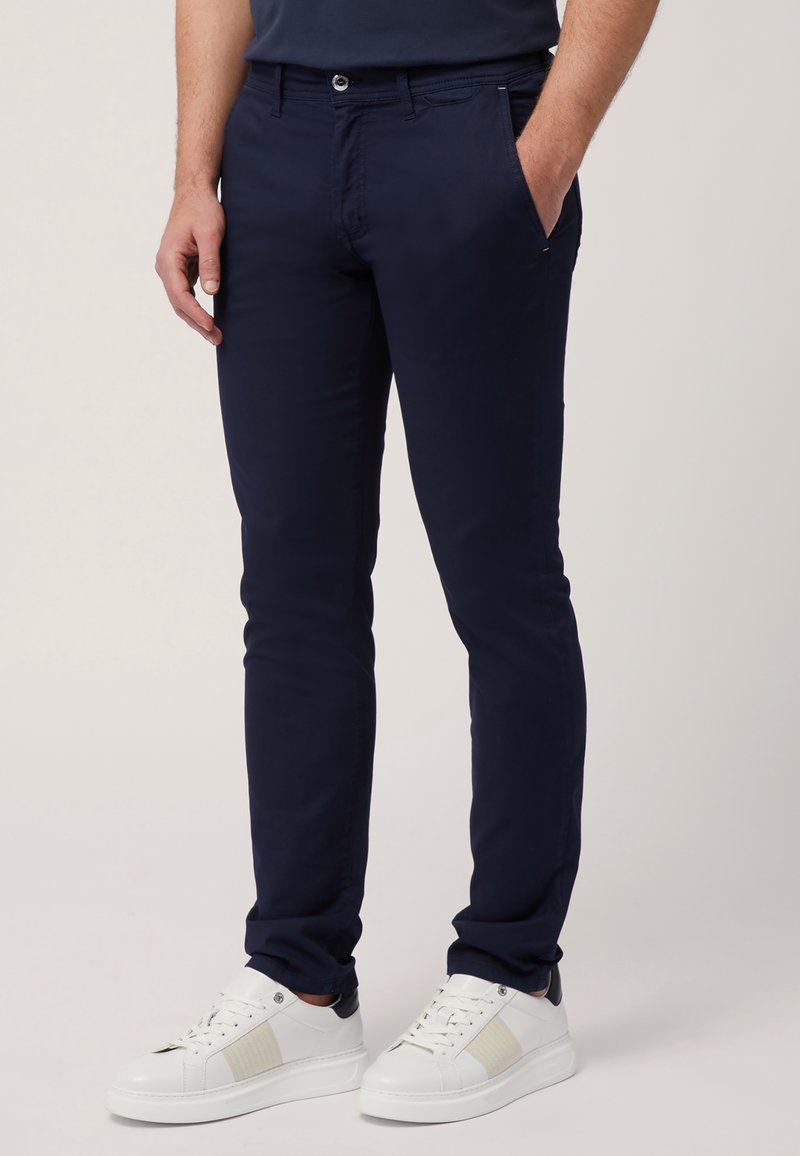 Náměrkové slim-fit chinos v hladké bavlněné tkanině, s bočními kapsami a předním zapínáním na knoflík. V kombinaci s bílými teniskami.