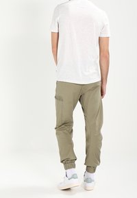 Ljust grå T-shirt ihop med olivgröna joggerbyxor med justerbar mudd, sidofickor och diskret tygstruktur. Sneakers fulländar looken.