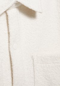 Valkoinen fleece-paita, jossa on teksturoitu pinta, klassinen kaulus, nappikiinnitys ja kaksi etutaskua.