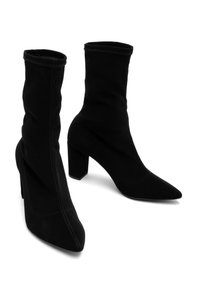Bottines noires en tissu doux, avec un bout slim et pointu et un talon épais. Couture décorative visible à la surface.