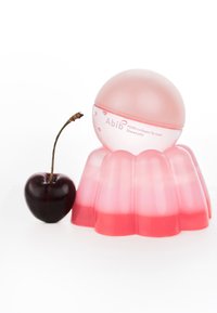 Masque pour les lèvres au collagène PDRN dans un récipient rond rose posé sur une base en gelée dégradée rose, à côté d'une cerise noire avec sa tige.