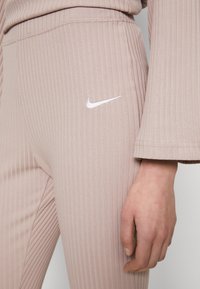 Ljust rosa ribbade leggings med en vit Nike-logga på låret. Tyget har en strukturerad yta, och midjan är åtsittande.