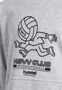 Grauer Pullover mit einem schwarzen Cartoon-Charakter, der Volleyball spielt, mit der Aufschrift "HSW CLUB INTERNATIONALS" und "hummel sportswear" darunter.