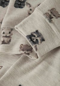 Heller beiger Stoff mit kleinen Tiermotiven, darunter Waschbären und Hasen, mit weicher Textur und sichtbaren Nähdetails.