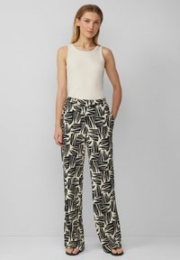 Witte geribde tanktop gecombineerd met wijde broek met een zwart bladmotief op een lichte achtergrond; beide materialen lijken zacht.