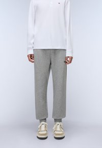Graue Jogginghose mit lockerer Passform, gerippten Bündchen und kleinem Logo. Kombiniert mit einem weißen Langarm-Polohemd und beigen Sneakern.