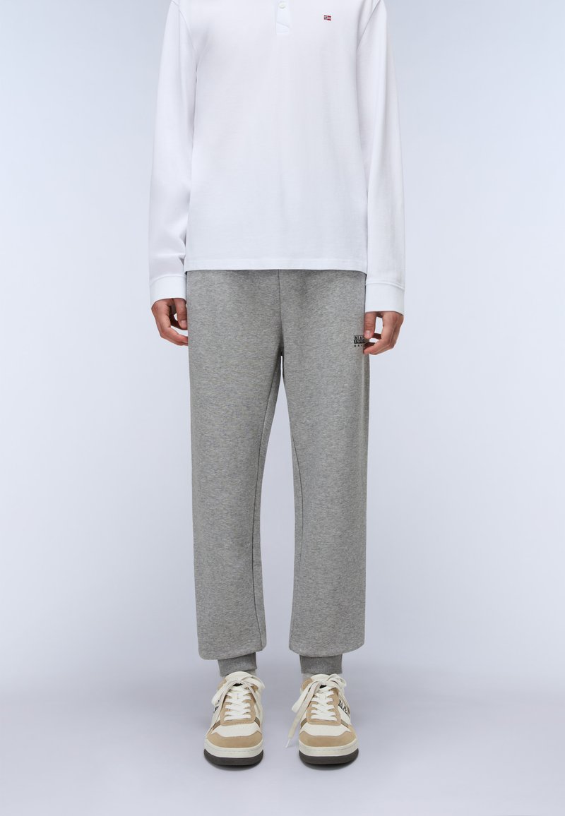 Graue Jogginghose mit lockerer Passform, gerippten Bündchen und kleinem Logo. Kombiniert mit einem weißen Langarm-Polohemd und beigen Sneakern.
