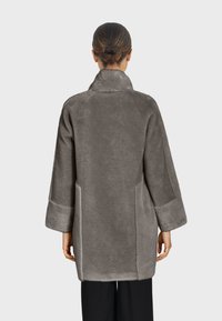 Sivi kaput od umjetnog krzna s reverima, dugim rukavima i bočnim džepovima. Mekana tekstura, dizajn do koljena i opušteni kroj.