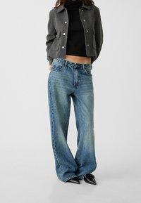 Gray cropped jacket with silver buttons, paired with light blue wide-leg jeans and black pointed-toe heels. Smooth fabric and relaxed fit.