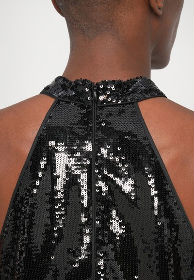 Μαύρο τοπ με αποκριάτικες παγιέτες και κλείσιμο με φερμουάρ στην πλάτη, με μαλακή υφή και λαμπερή, ανακλαστική επιφάνεια.