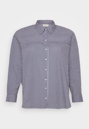 Camisa de botão às riscas com mangas longas, apresentando linhas verticais em azul-marinho e branco, um colarinho clássico e uma bainha reta. Detalhes com botões na parte da frente.