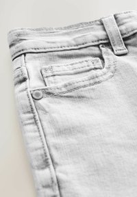Grå denimjeans med en texturerad yta. Har en liten bakficka, bältesömmar och sydda detaljer längs sömmarna.