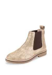 Bota Chelsea de ante beige brillante con un panel lateral elástico marrón y una tira de agarre, que presenta una punta redondeada y una suela de goma baja.