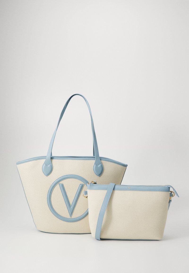 Two bags: a large cream tote with a blue leather trim and a circular logo, and a smaller cream pouch with a detachable blue strap.