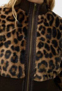 Giacca in pelliccia sintetica con stampa leopardo e colletto a coste marrone. Presenta una cerniera dorata e una texture morbida, combinando pelliccia e tessuto liscio.