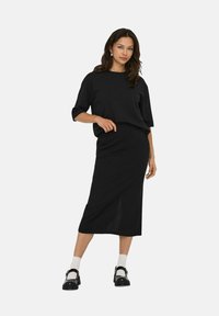 Svart stickad topp med korta ärmar, kombinerad med en svart midi-kjol. Har en avslappnad design och slät textur. Svarta klumpiga skor fulländar looken.