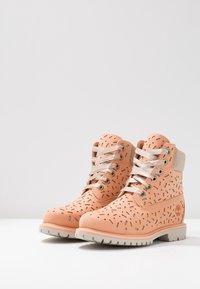 Stivali alla caviglia color pesca con motivi traforati, suola in gomma crema, design con lacci argentati e colletto imbottito per il comfort.