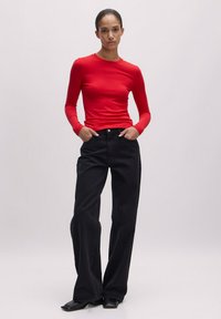 Rotes, geripptes Langarmshirt, kombiniert mit hoch taillierten, schwarzen, weiten Jeans. Das Outfit zeichnet sich durch eine schmale Passform und glatte Texturen aus.
