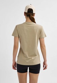 Beige bomulds T-shirt med korte ærmer, en afslappet pasform og rund halsudskæring, parret med sorte shorts. Simpelt design, ingen synlige mønstre.