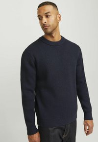 Marineblauer gerippter Strickpullover mit rundem Halsausschnitt, langen Ärmeln und geradem Saum. Strukturiertes Gewebe mit leichtem Stretch. Getragen mit dunklen Jeans.