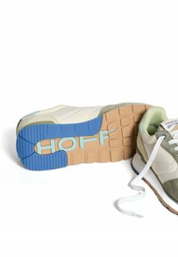 Zapatilla deportiva con un upper acolchado blanco, detalles en ante verde, suela de goma beige y azul, y la marca "HOFF" en un azul claro.