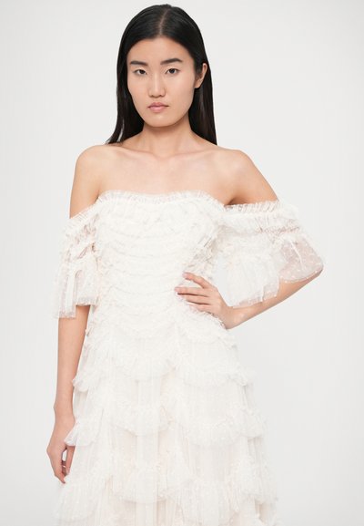 Off-the-shoulder white dress with layered ruffles, made from sheer fabric. Puff sleeves with frill details and dotted texture.