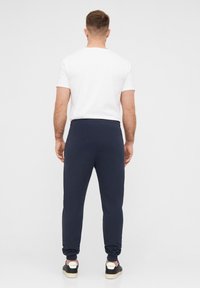 Marineblaue Jogginghosen mit elastischem Bund und Bündchen, kombiniert mit einem schlichten weißen T-Shirt und schwarzen Sneakers mit weißen Akzenten.