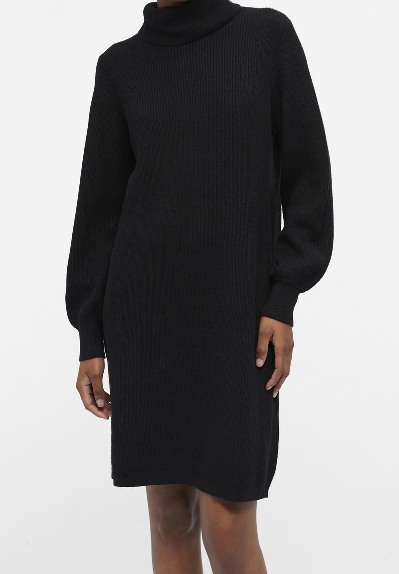 Schwarzes Strickkleid mit Stehkragen, langen Puffärmel, geripptem Muster und seitlichen Schlitzen. Es verfügt über eine lockere Passform und ein knielanges Design.