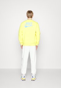 Jasně žlutá mikina s modrým logem Nike na zádech, doplněná o bílé tepláky a vícebarevné tenisky. Jednoduchý design.