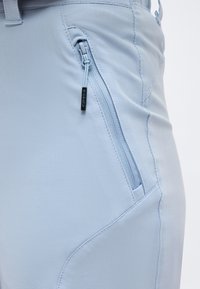 Κοντινό πλάνο σε ανοιχτό μπλε παντελόνι που δείχνει την μπροστινή τσέπη με φερμουάρ, διαθέτοντας υφασμάτινη ταινία έλξης και λεπτομερή ραφή.