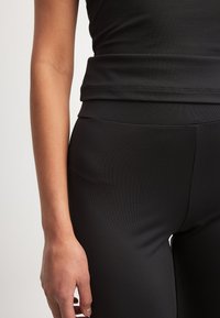 Melnas sporta apģērba augšdaļas un pieguļoši legingi, izgatavoti no gludas, elastīgas materiāla. Iespējams bezšuvju dizains ar teksturētu apdari.