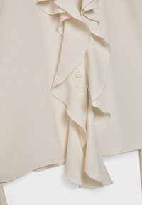 Blouse couleur crème avec des détails volantés sur le devant, une fermeture à boutons et une texture lisse et légère.