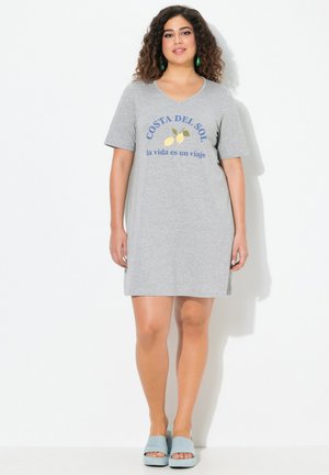Graues Baumwoll-T-Shirt-Kleid mit kurzen Ärmeln, das einen grafischen Aufdruck von "Costa del Sol" und Zitronen sowie seitliche Schlitze aufweist. Kombiniert mit blauen Rutschsandalen.