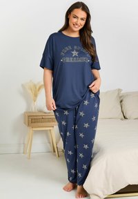 Mörkblå pyjamas-set bestående av en lös t-shirt med texten "FREE SPIRIT DREAMER" och byxor med stjärnmönster. Mjuk stoff, avslappnad passform.