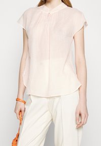 Blusa rosa chiaro a maniche corte con colletto alla cinese e chiusura a bottoni. Realizzata in un tessuto leggero e trasparente con una vestibilità morbida.