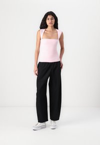 Top de tirantes ajustado color rosa claro con escote cuadrado y mangas cortas, combinado con pantalones negros holgados y zapatillas blancas. Textura suave en general.