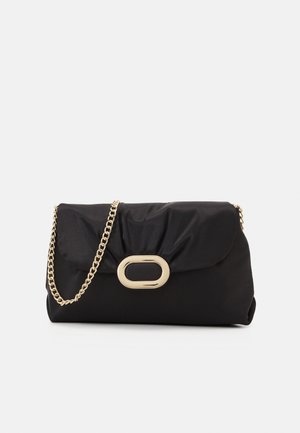 Sac pochette noir avec un fermoir ovale doré et une bandoulière chaîne dorée sur un fond uni clair.
