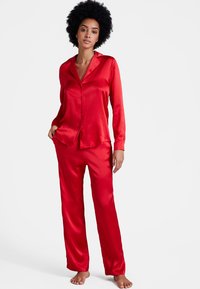 Ensemble de pyjama en satin rouge comprenant une chemise à manches longues avec boutons et col, ainsi que des pantalons assortis, texture lisse et coupe décontractée.